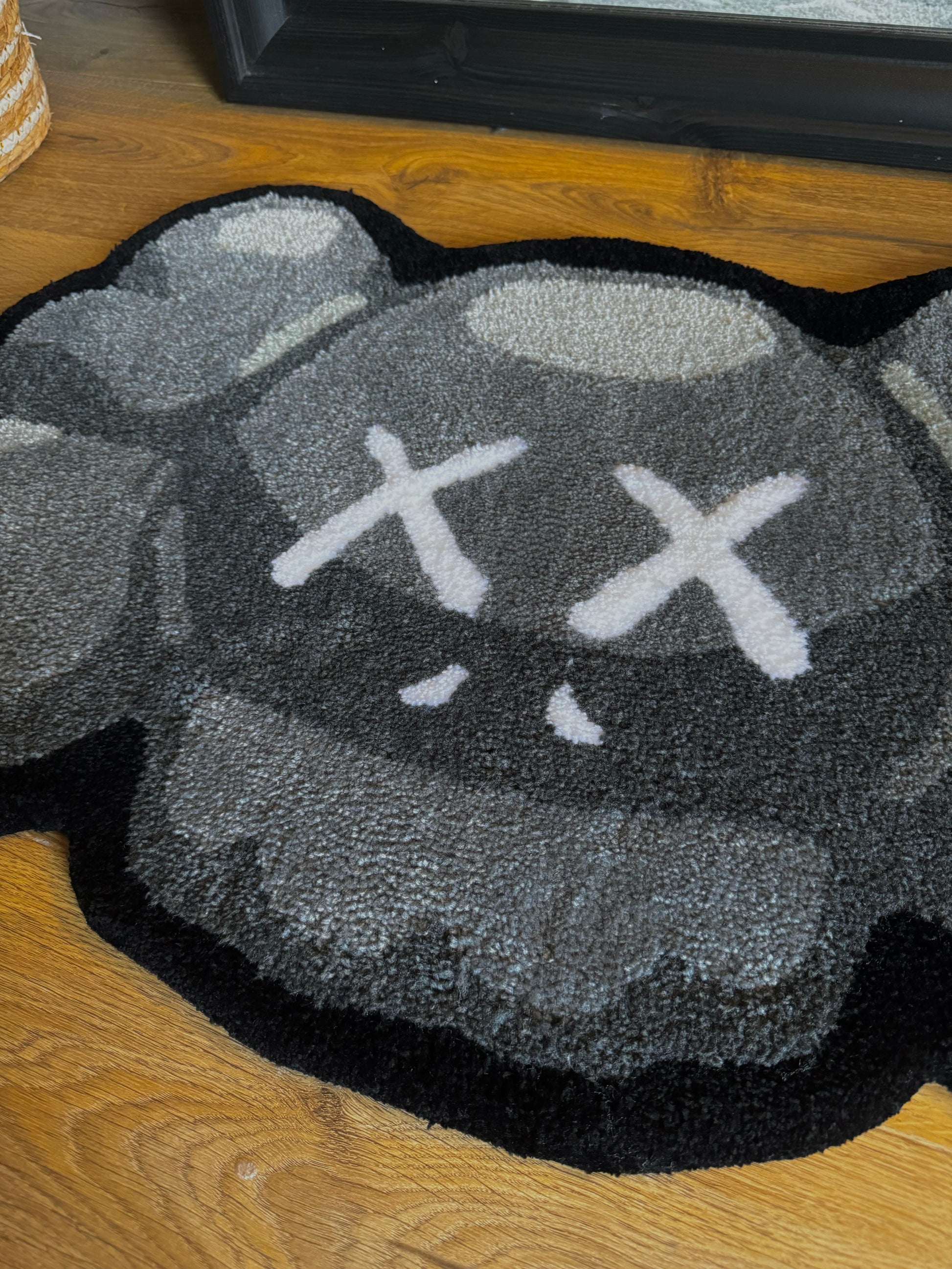 A handmade KAWS face tufted rug with a gray and black color scheme, featuring a stylized character face.